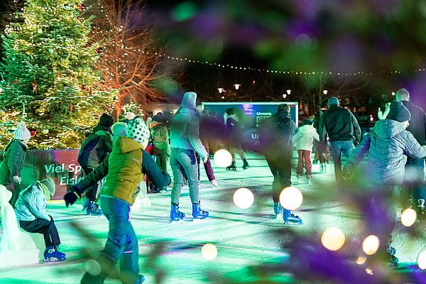 Eisdisco auf dem Merseburger Markt Im Bild sind Menschen zu sehen, die auf einer beleuchteten Eisbahn Schlittschuh laufen.
